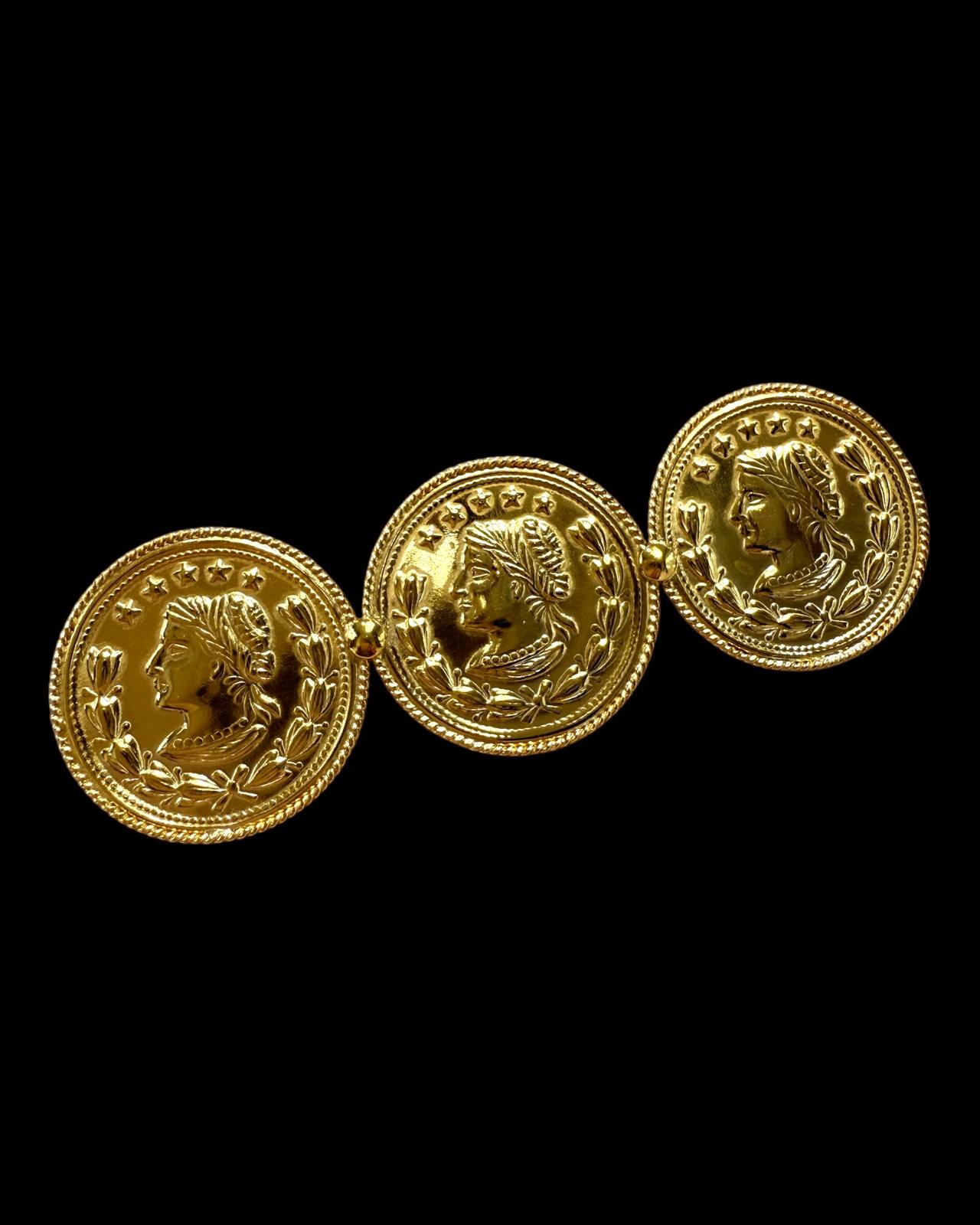 Alfinete em prata dourada com três moedas gravadas com figuras femininas e folhas de louro.