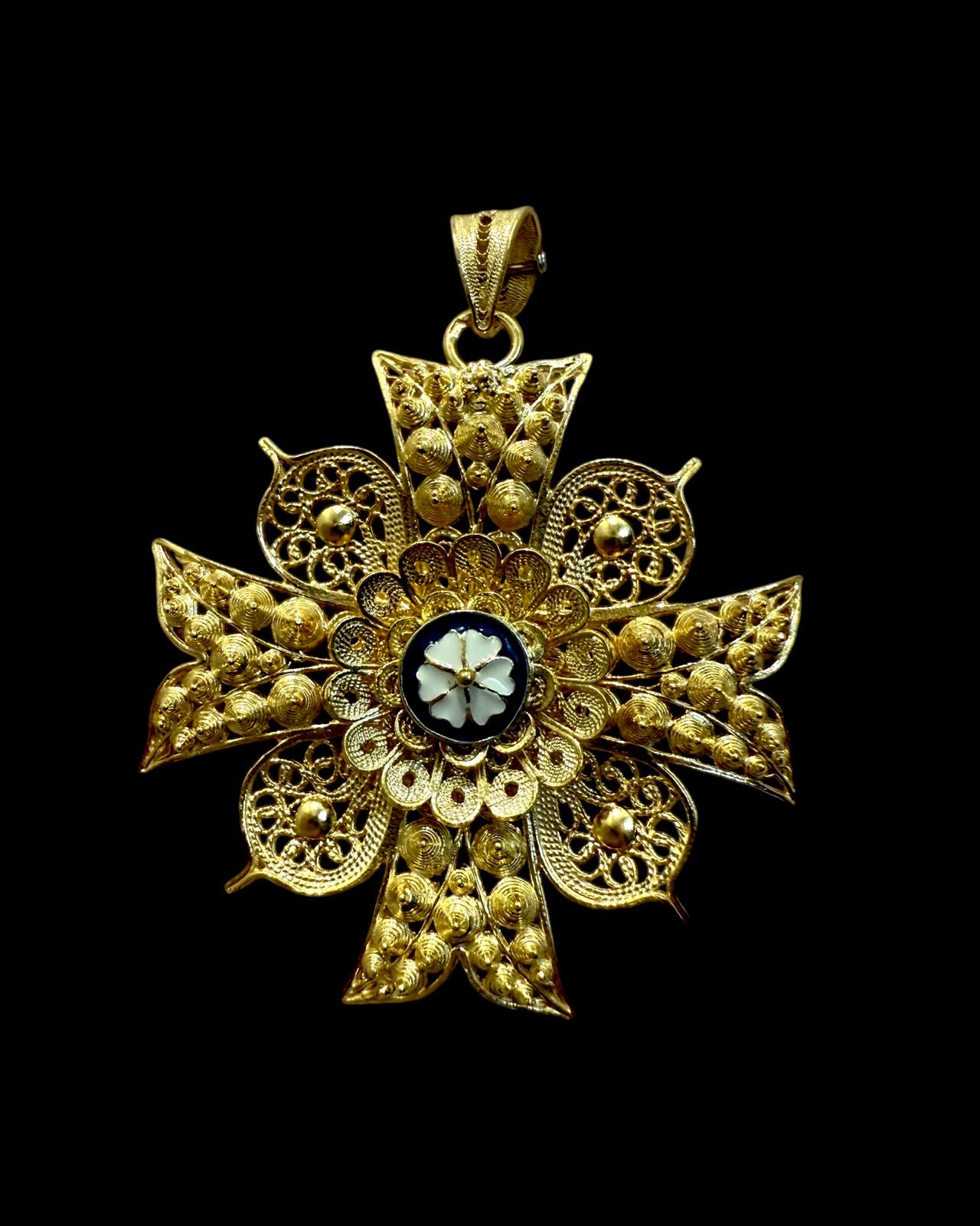 Medalha pequena em forma de Cruz de Malta com filigrana dourada, flor em esmalte branco e contorno azul ao centro
