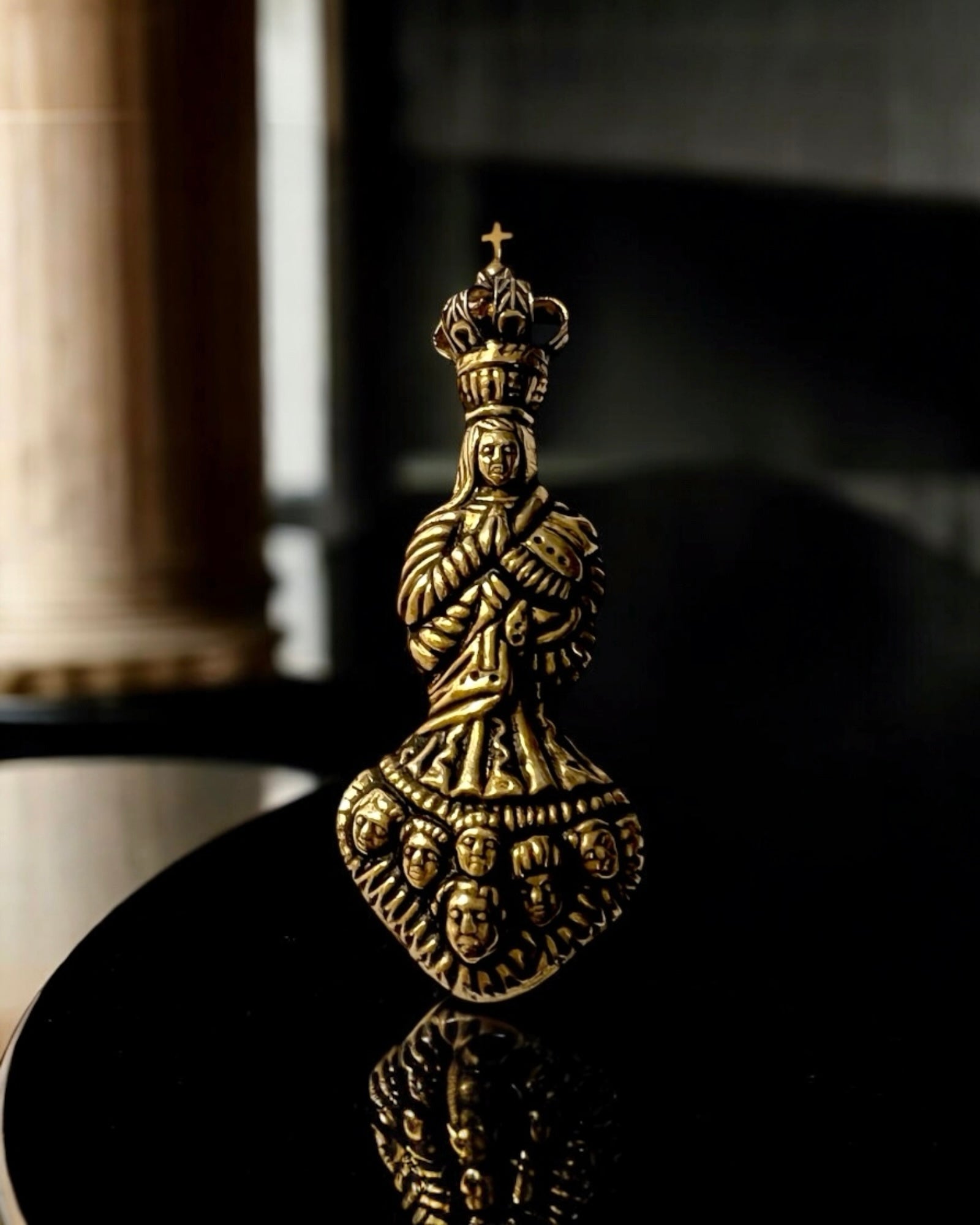 Medalha da Nossa Senhora do Caneco em prata dourada com acabamento barroco e detalhe de rostos esculpidos.
